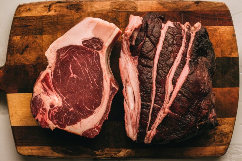 A beautifully marbled chuck steak and a perfect naval end briske sit on a rustic wooden cutting board, showcasing their rich textures and inviting colors, ready to be transformed into a gourmet burger mince.