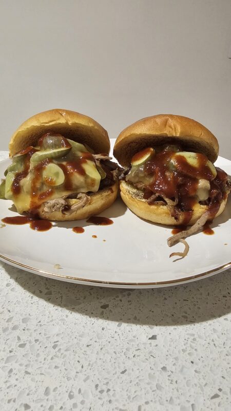 Smoked Pulled Pork Buns with jalapenos, melted cheese and BBQ sauce on a white plate on a stone counter top