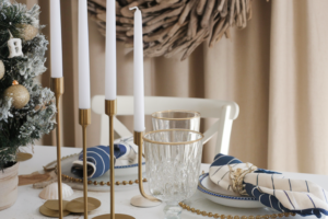 Coastal chic Christmas table setting with nautical elements, gold accents, and a driftwood wreath for a stylish holiday gathering.